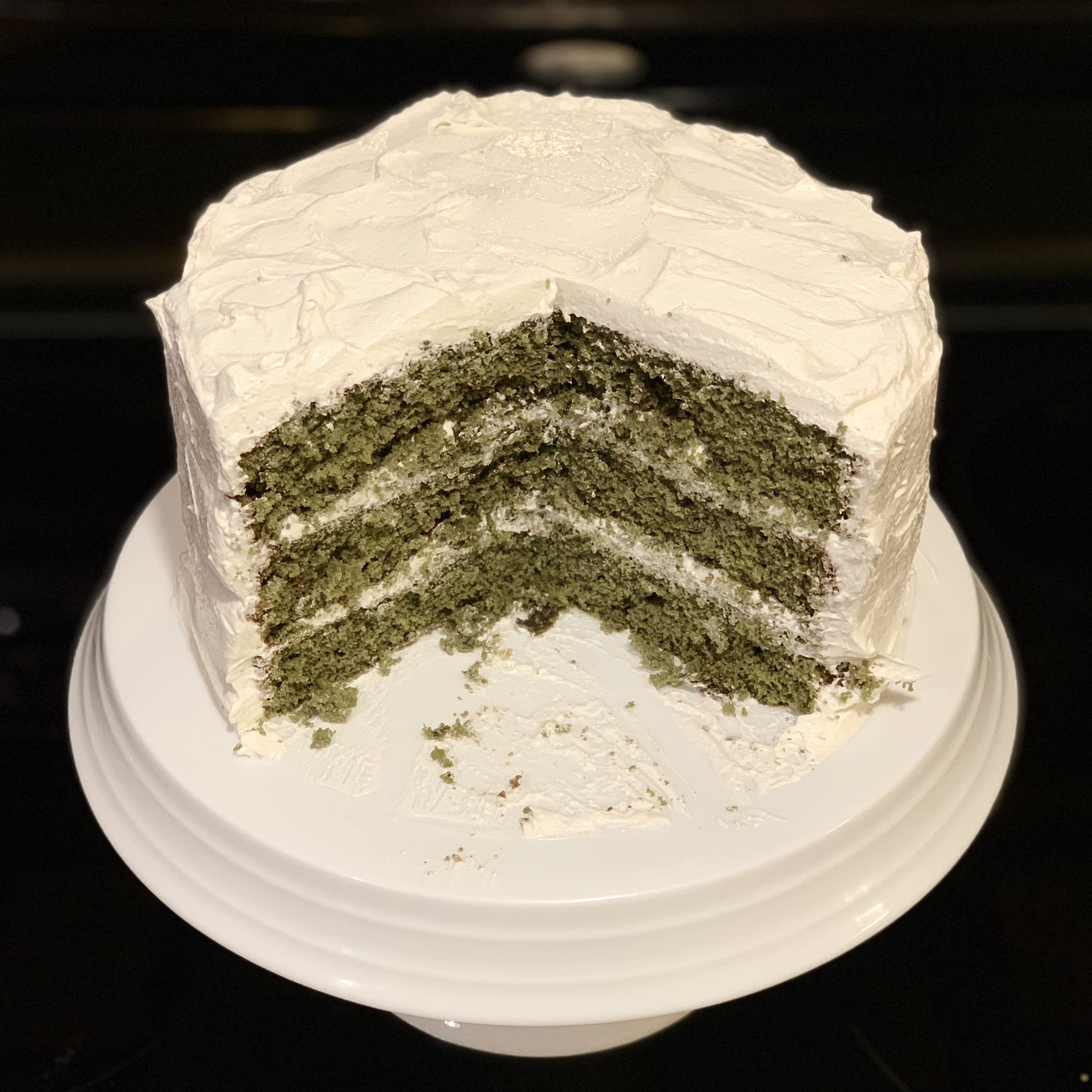 Green cake with white icing on a white cake stand